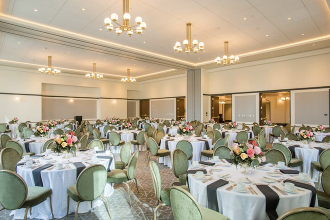 The ballroom at the Laura Hotel with chandeliers, white linens and green chairs. 